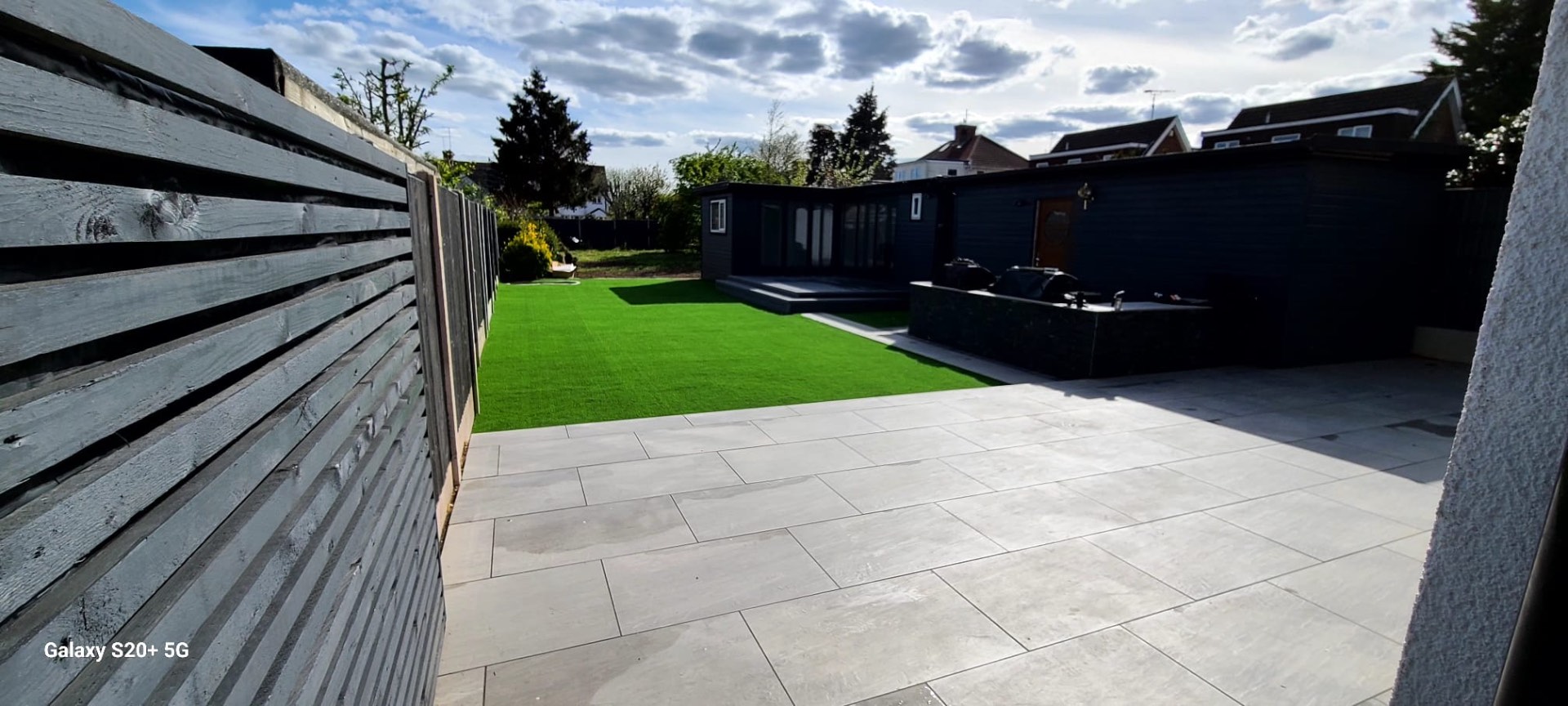 View across a porcelain patio to a navy garden room, framed by a slatted fence