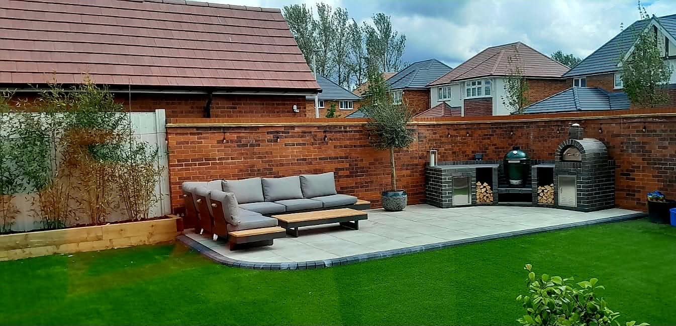 Brick outdoor kitchen with pizza oven beside a porcelain patio and artificial lawn, built by Golden Hands